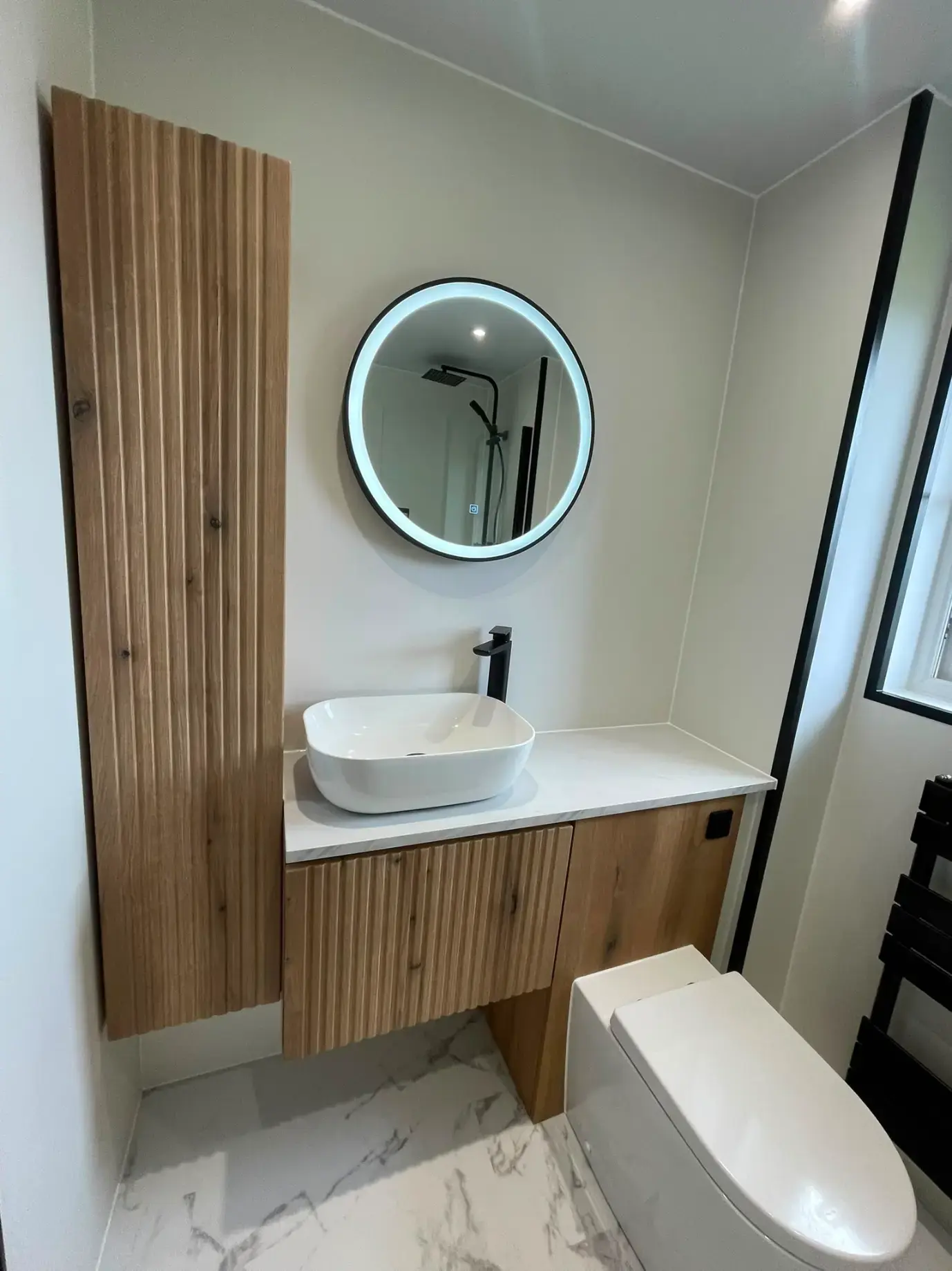 Fluted wood vanity and tall cabinet with round illuminated mirror