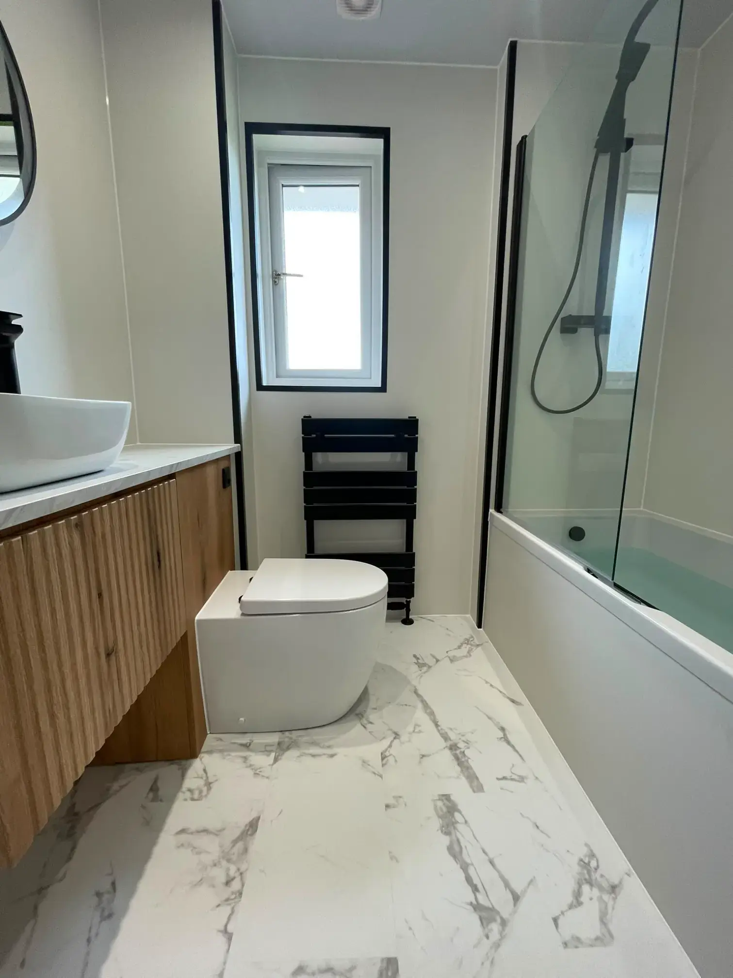 Fluted wood furniture beside a bath with black shower fittings